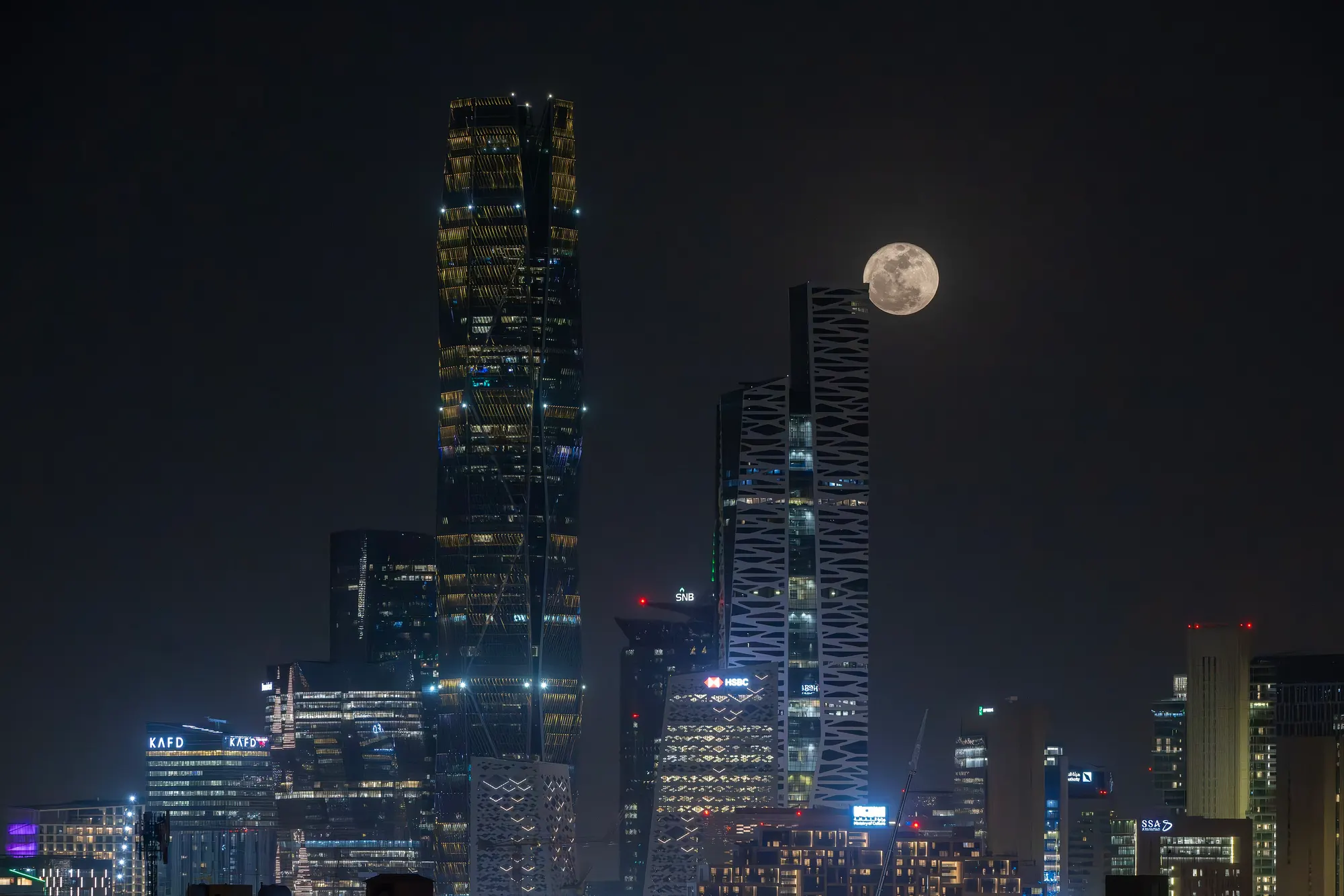 The King Abdullah Financial District lit at night with a full moon beside the tallest tower