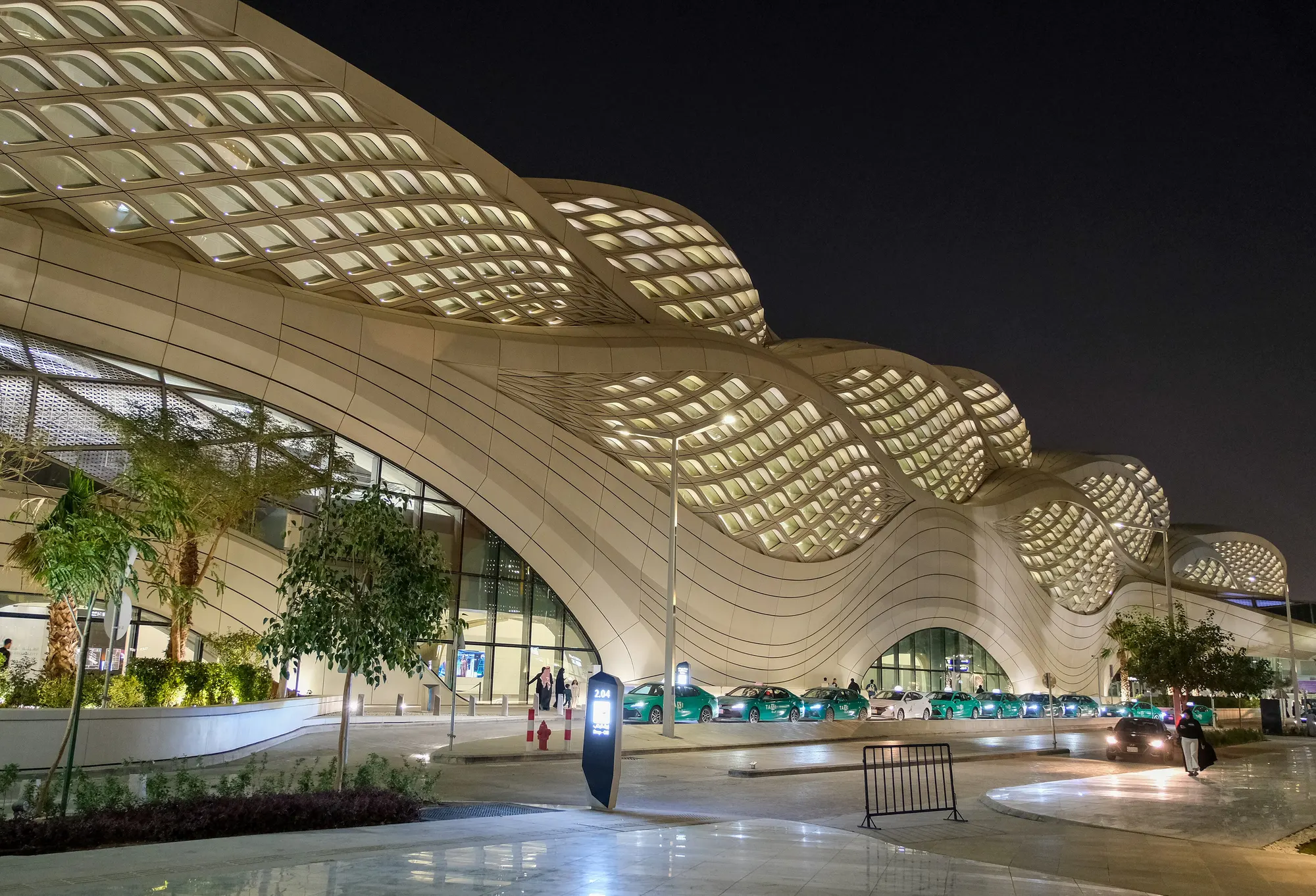 The KAFD metro station canopy lit warm white at night, its lattice rippling over the entrance