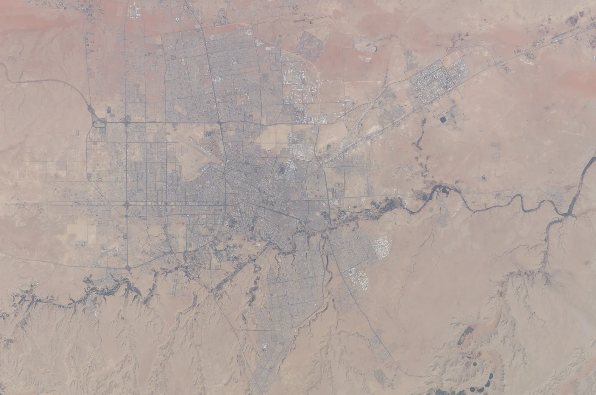 Riyadh seen from orbit by day: the city grid spreading over the desert, crossed by a dry riverbed